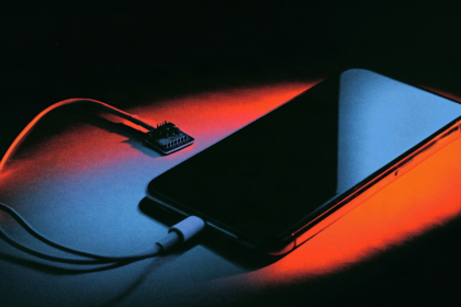 Risograph illustration of a thumbnail-sized circuit board cabled to a phone lying on a workbench